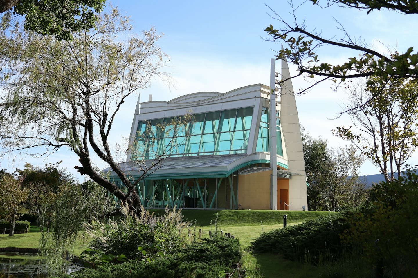 Modern building with a wavy roofline overlooks a garden pond.