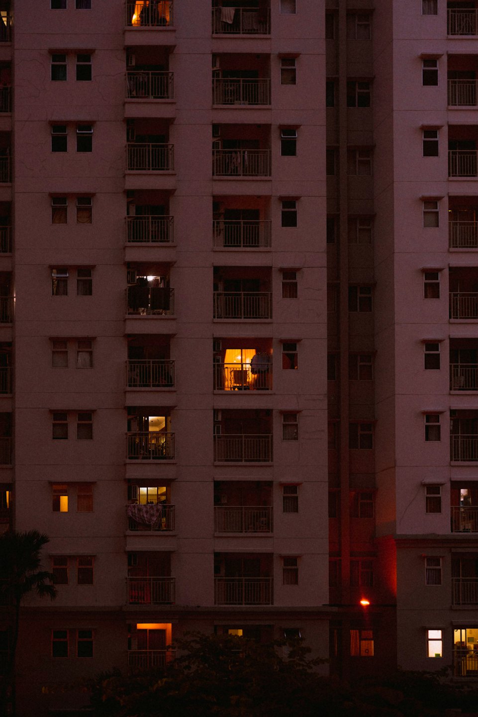 Glowing windows illuminate the facade of a tall apartment building.
