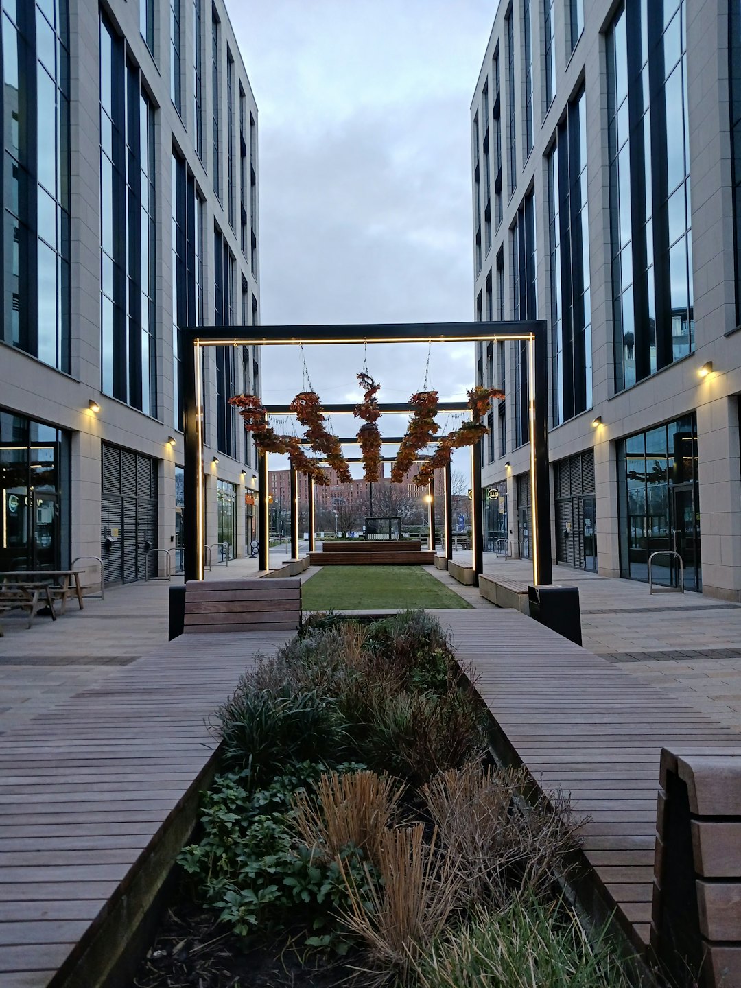 Modern courtyard with wooden pathways and decorative archway at dusk.